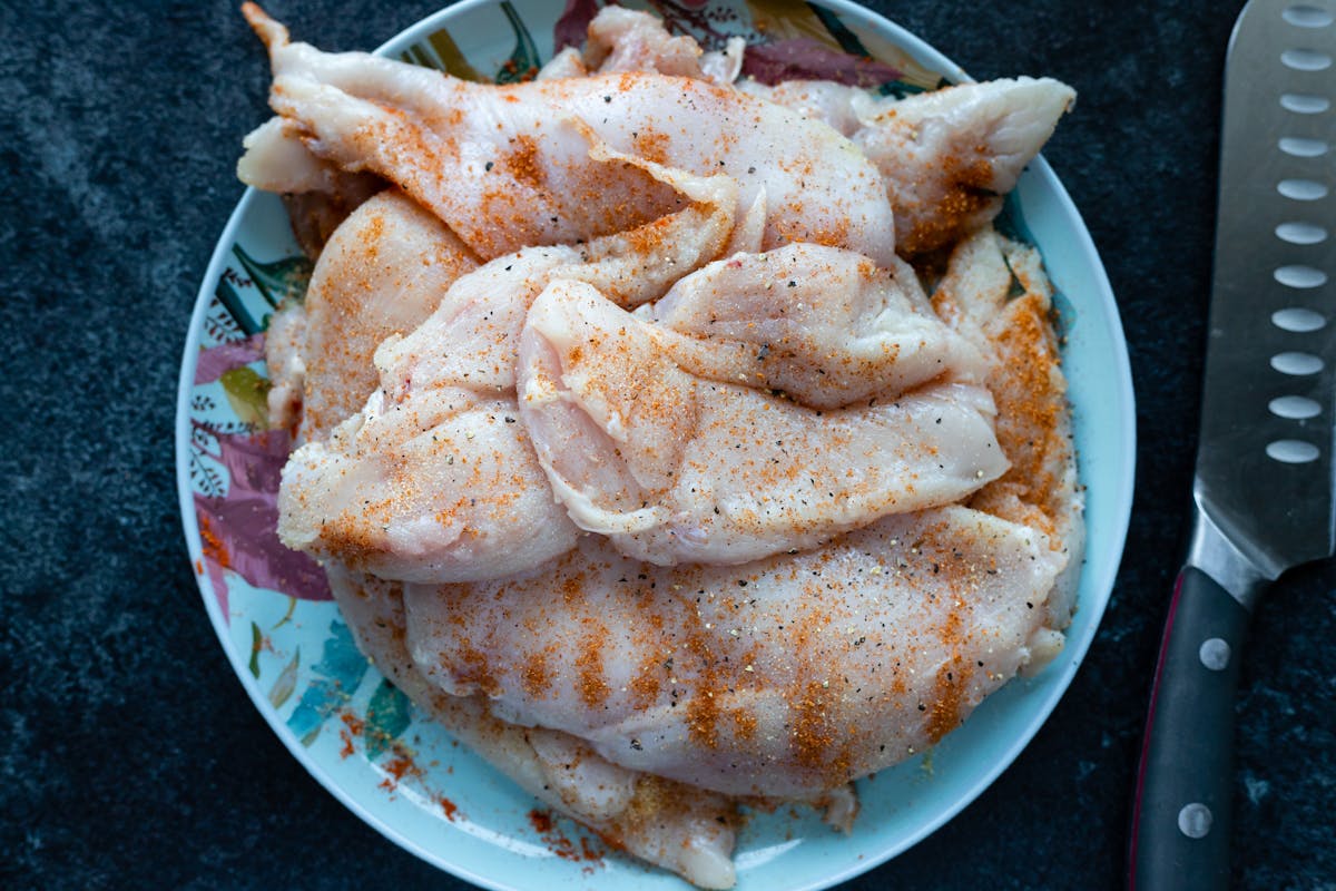 Raw chicken breasts on a plate ready for refrigerator storage, showing proper fridge thaw prep for frozen chicken